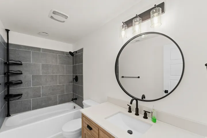 White countertop with an undermount sink, wood-finish vanity, and matte black fixtures