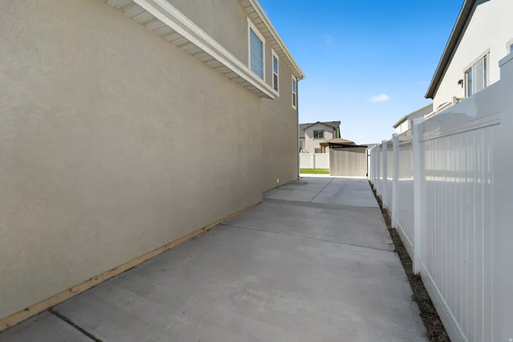 Concrete pathway featuring a stucco exterior wall and white panel fencing