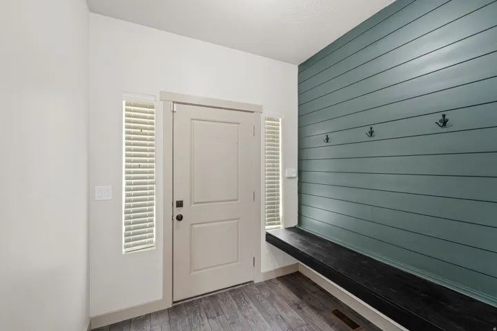 Entryway featuring a built-in dark wood-finish bench, shiplap accent wall, three coat hooks, and wood-finish flooring