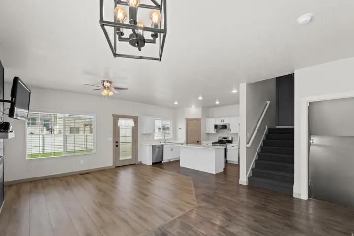 Open-concept living space featuring wood-finish flooring, a contemporary chandelier, recessed lighting, and a kitchen with an island, white cabinetry, and stainless steel appliances