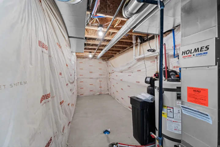 Unfinished basement with concrete flooring and exposed ceiling joists, featuring a furnace, water heater, and water softener