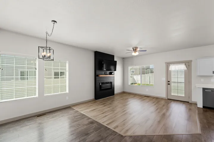 Open-concept living area featuring two-tone wood-finish flooring, a modern black fireplace surround with an electric insert, and a ceiling fan