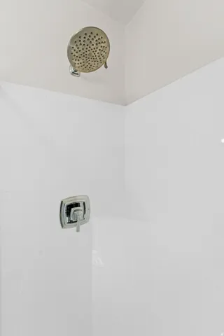 White subway tile shower enclosure with a built-in corner shelf, chrome showerhead, and a square chrome handle