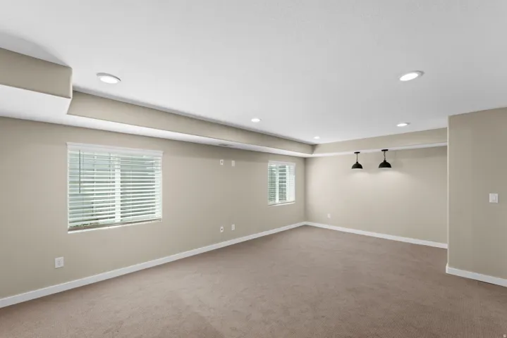 Recessed lighting, neutral wall tones, two windows with blinds, two wall-mounted pendant lights, and carpet flooring