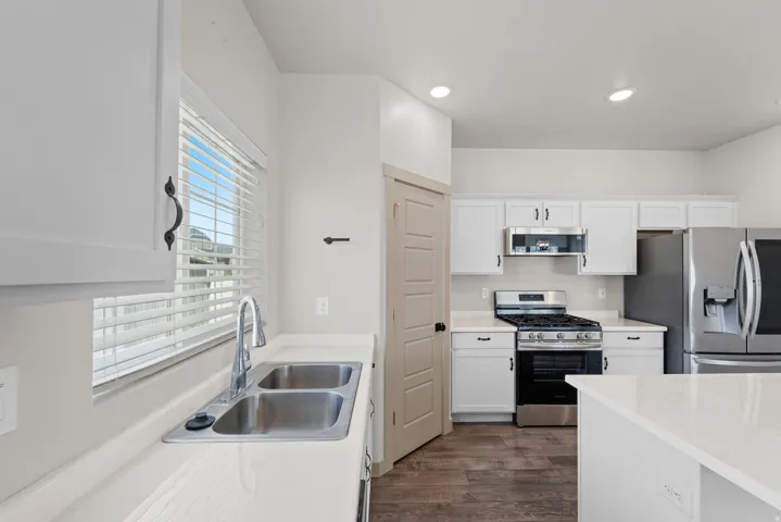 Kitchen featuring white cabinetry, stainless steel appliances, a double basin sink, light-toned countertops, and wood-finish flooring