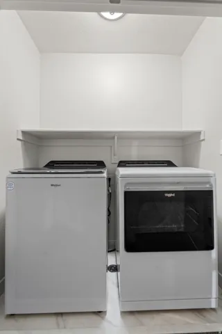 Dedicated laundry space with a built-in shelf, overhead lighting, and tiled flooring
