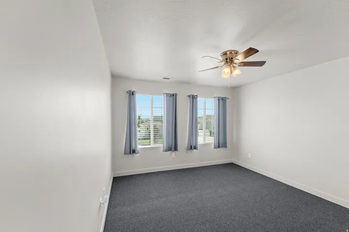 Carpeted flooring, three windows with blinds, ceiling fan with integrated lighting