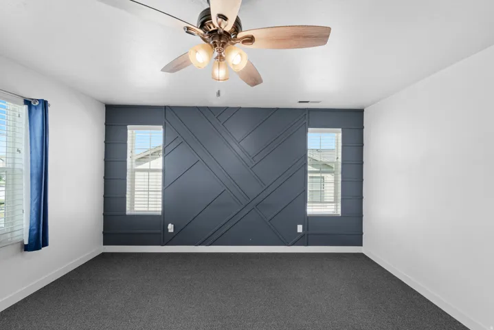 Accent wall with geometric paneling, ceiling fan with integrated lighting, carpeted flooring, and multiple windows