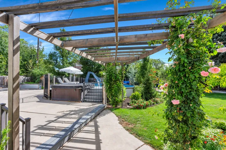 Expansive pergola structure with climbing roses and lush greenery, concrete patio, built-in spa, and a landscaped lawn area