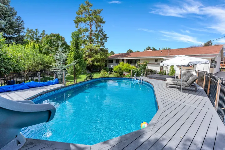 Expansive backyard featuring a large swimming pool with slide, composite decking, and mature landscaping