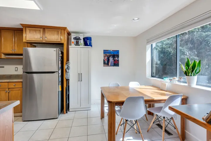Kitchen with wood cabinetry, stainless steel refrigerator, white tiled flooring, and recessed lighting