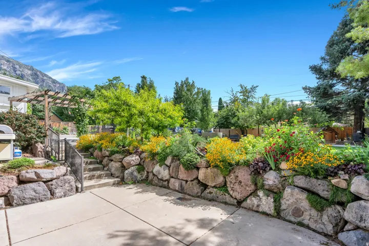 Concrete patio with a stone retaining wall, staircase with metal railings, and a wooden pergola structure