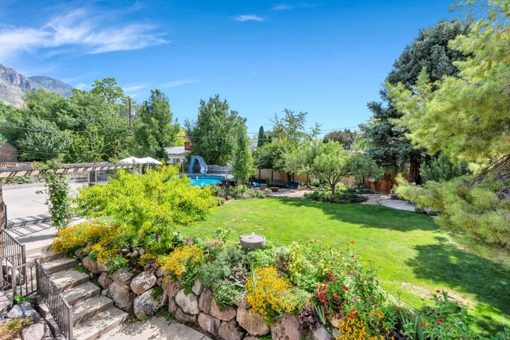 Expansive backyard featuring a manicured lawn, established landscaping, stone retaining walls, and a swimming pool