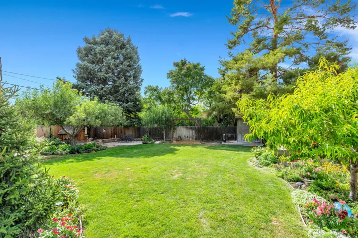 Expansive backyard with a manicured lawn, established garden beds, mature trees, and privacy fencing
