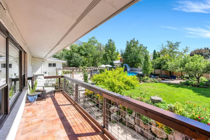 Outdoor balcony with brick tile flooring and metal railing overlooking a spacious green lawn