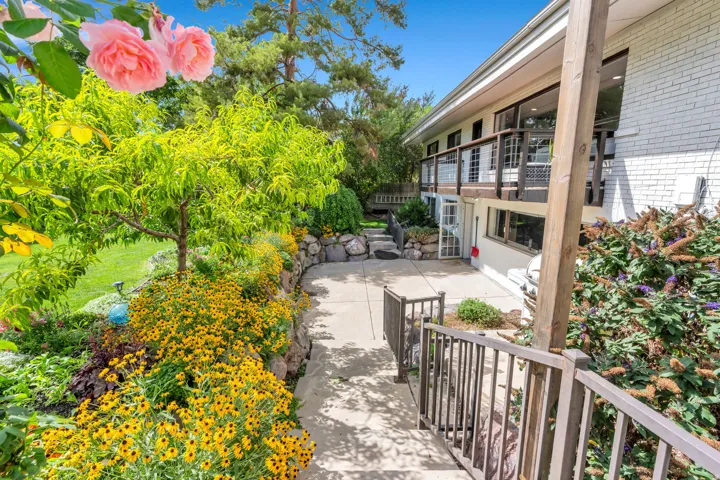 Concrete patio with a stone retaining wall, mature landscaping, and a multi-level wood deck