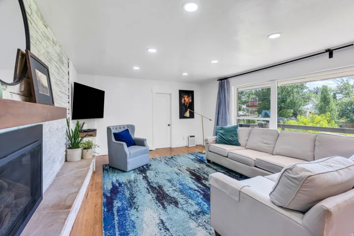 Recessed lighting, wood-finish flooring, white brick-style fireplace surround, wood mantel, and expansive windows