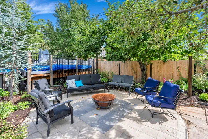 Paved patio with a central fire pit, surrounded by mature trees and landscaped planting beds