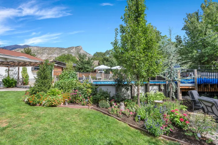 Expansive green lawn, mature trees, vibrant garden beds, and an above-ground pool with surrounding decking