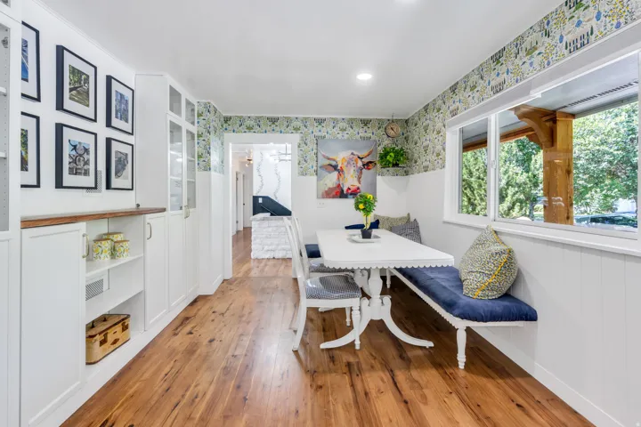 Wood-finish flooring, built-in white cabinetry with glass inserts, white wainscoting, and a built-in bench with a white dining table