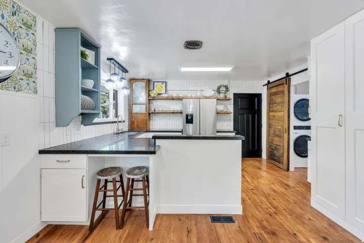 Wood-finish flooring, white cabinetry, dark countertops, and a barn door
