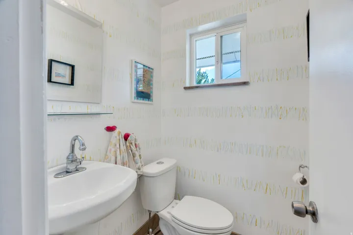 Pedestal sink with chrome faucet, wall-mounted mirror, built-in shelf, and a window with a wood sill