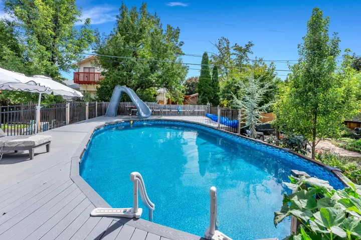 Expansive outdoor space featuring a kidney-shaped pool with a deck surround, black metal fencing, and mature trees