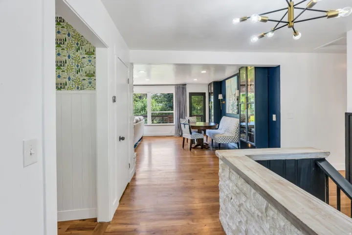 Wood-finish flooring throughout, white wall paneling, built-in shelving with accent lighting, contemporary chandelier, and stone-clad railing