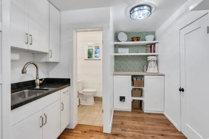 White cabinetry with brushed nickel hardware, black speckled countertop, undermount stainless steel sink with gooseneck faucet, and wood-finish flooring