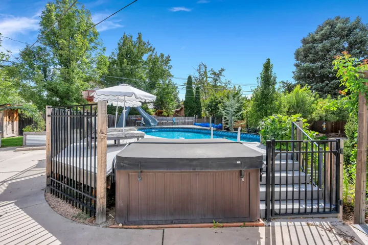 Fenced swimming pool with a water slide, adjacent hot tub, and surrounding mature trees