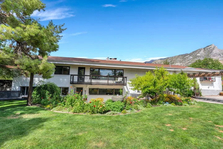 Expansive backyard with a manicured lawn, established garden beds, upper-level balcony, and mountain scenery