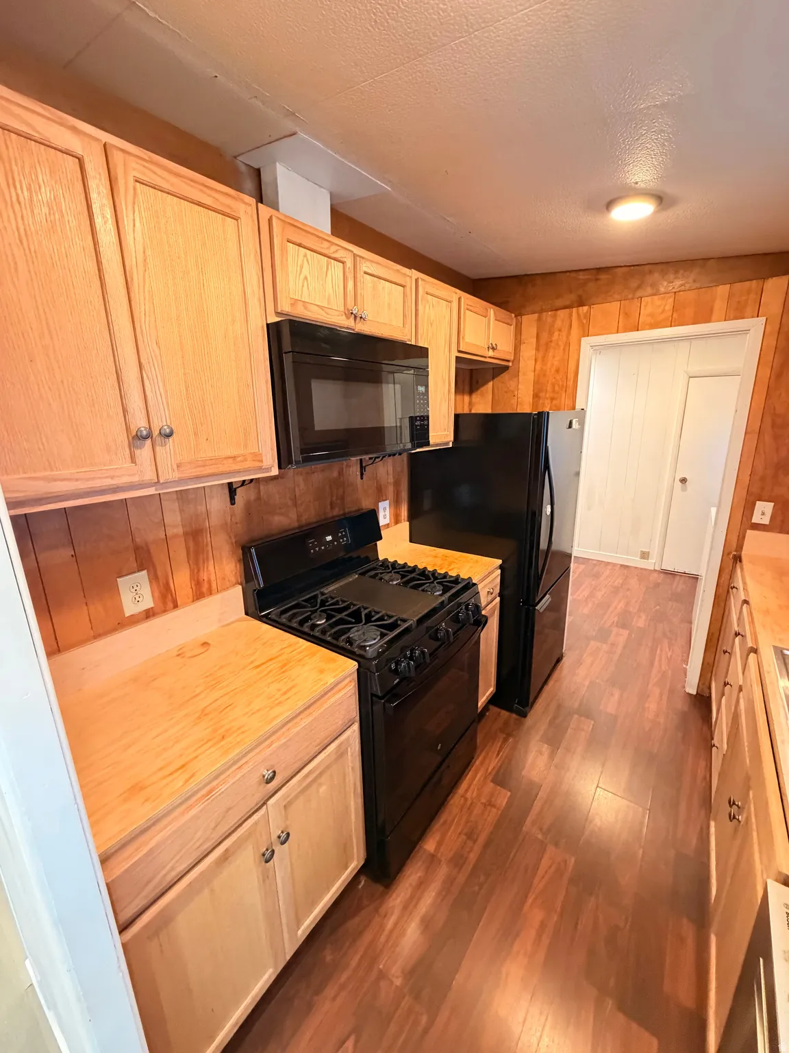 Wood-finish flooring with light wood cabinetry, black appliances, and paneling
