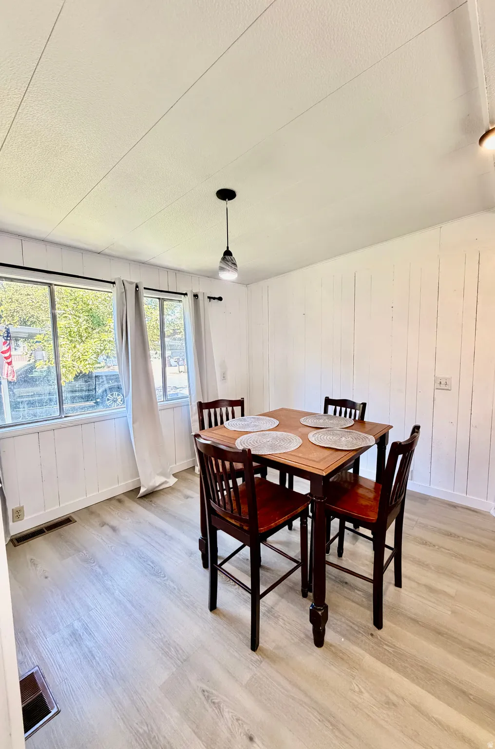 Light wood-finish flooring, white paneled wall finishes, and a contemporary pendant light fixture