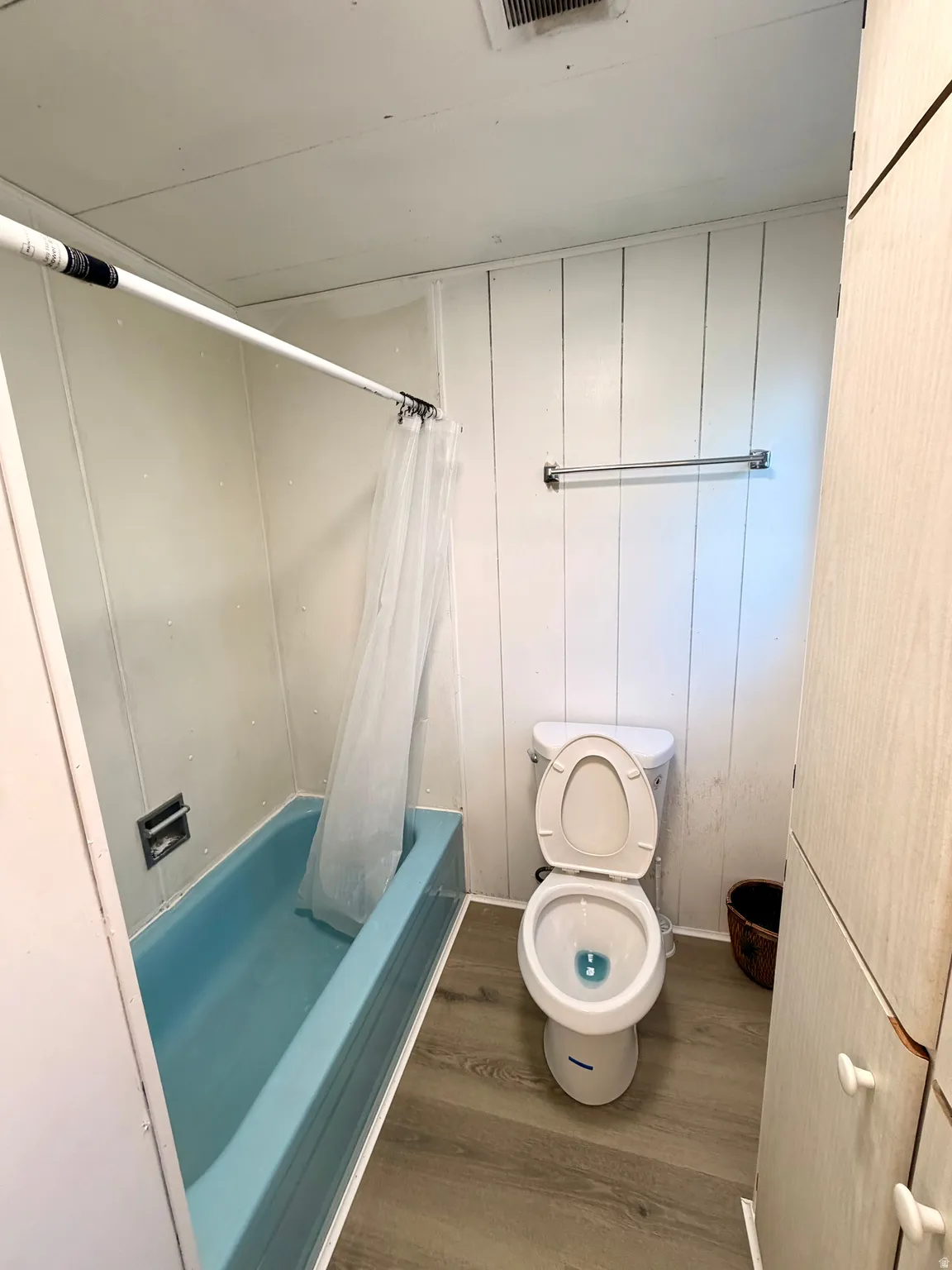 Wood-finish flooring, white paneled walls, built-in storage cabinetry, and a full bathtub