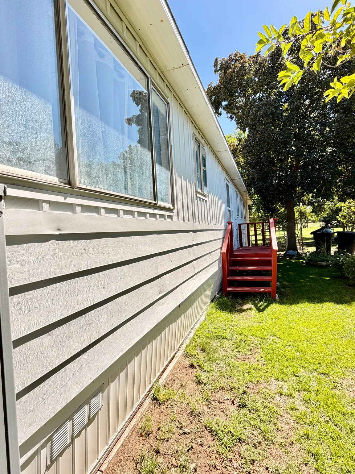 Light-colored siding exterior with contrasting red wood steps, multiple windows, and a green grass area