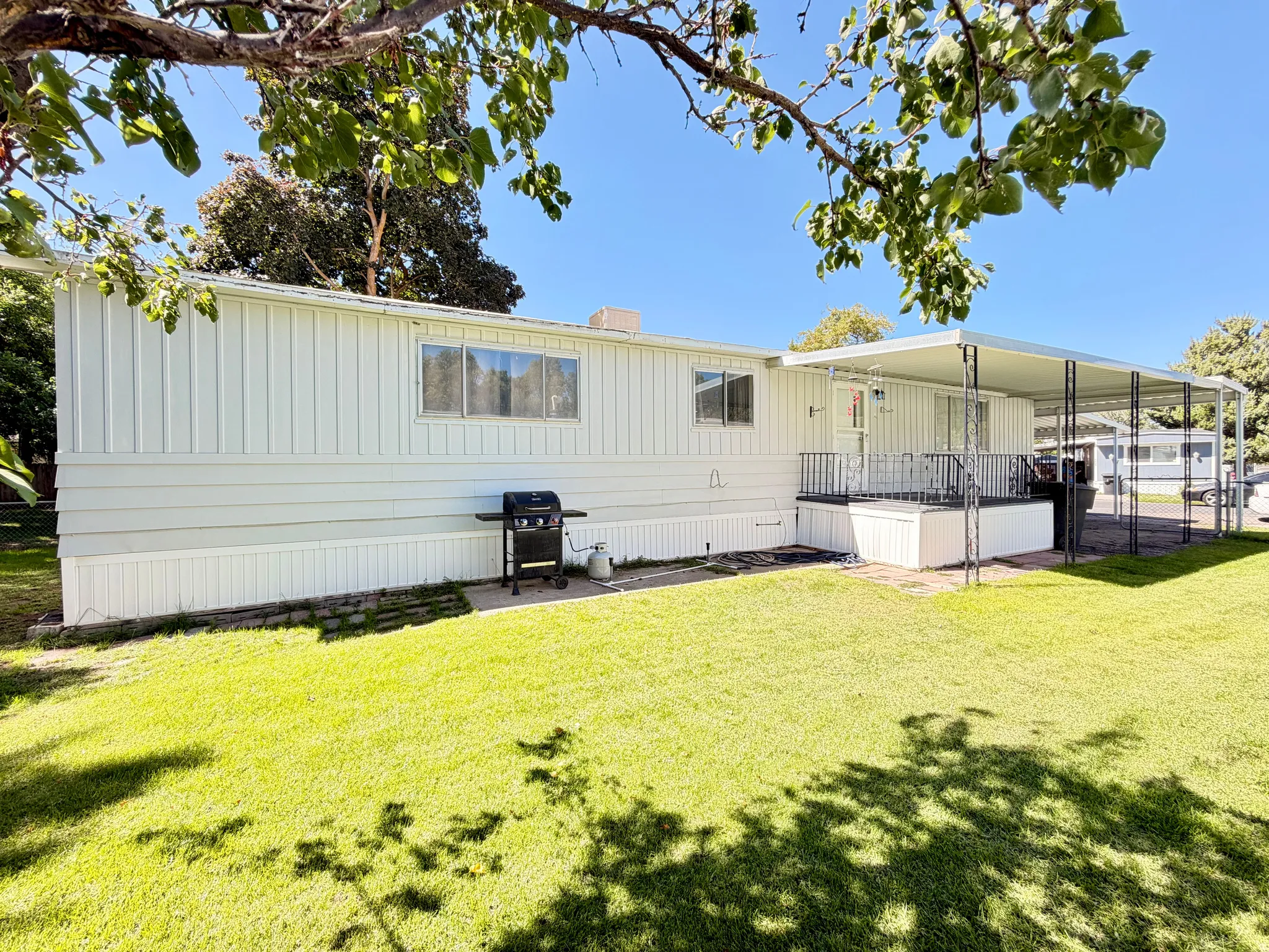 White horizontal siding exterior with a covered patio, metal patio railing, and a carport