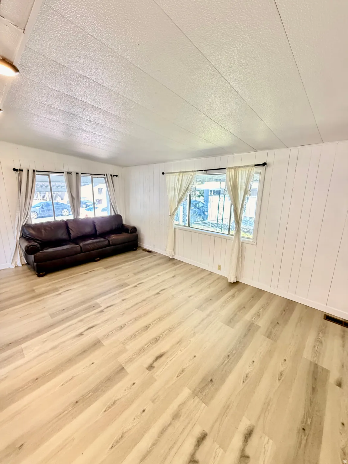 Wood-finish flooring throughout, white vertical paneling on walls, and multiple windows with white trim