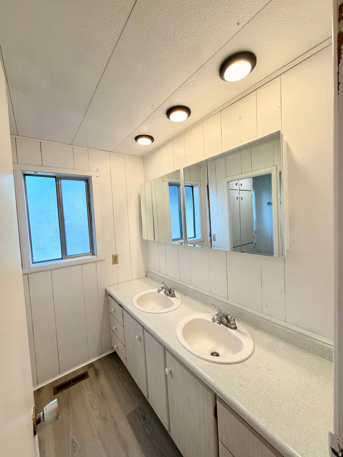 Dual basin vanity with extensive under-sink storage, laminate countertops, and multiple mirrored medicine cabinets