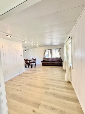 Light wood-finish flooring throughout, white vertical paneling, recessed ceiling lighting, and windows with white trim