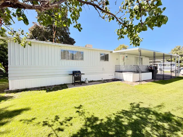 White horizontal siding exterior with a covered patio, metal patio railing, and a carport