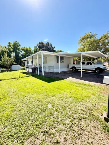 Expansive green lawn, white siding property, covered carport, chain-link fencing, and a separate storage shed