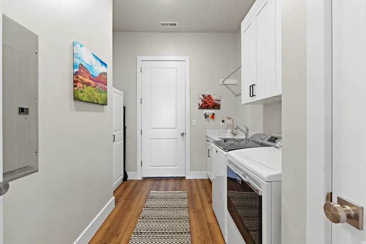 Wood-finish flooring with white baseboards, white shaker-style cabinetry, and a utility sink