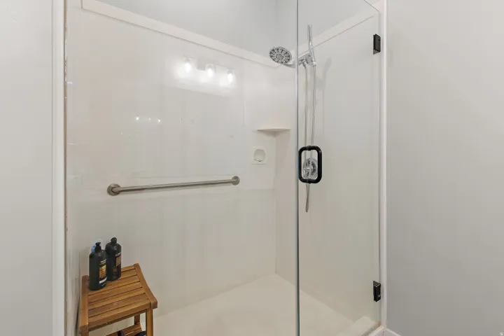 Walk-in shower with clear glass enclosure, white panel surround, built-in grab bar, and a handheld shower fixture