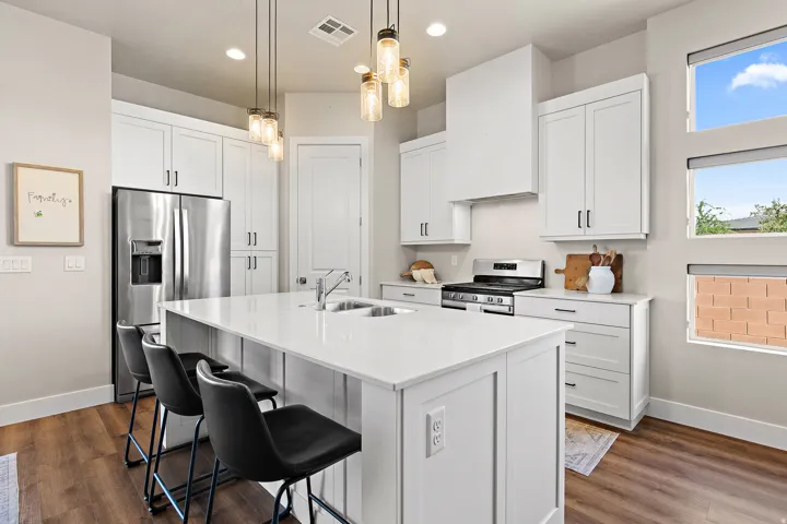 Modern kitchen featuring white cabinetry, stainless steel appliances, a large center island with an undermount double sink, wood-finish flooring, and multiple windows providing natural light
