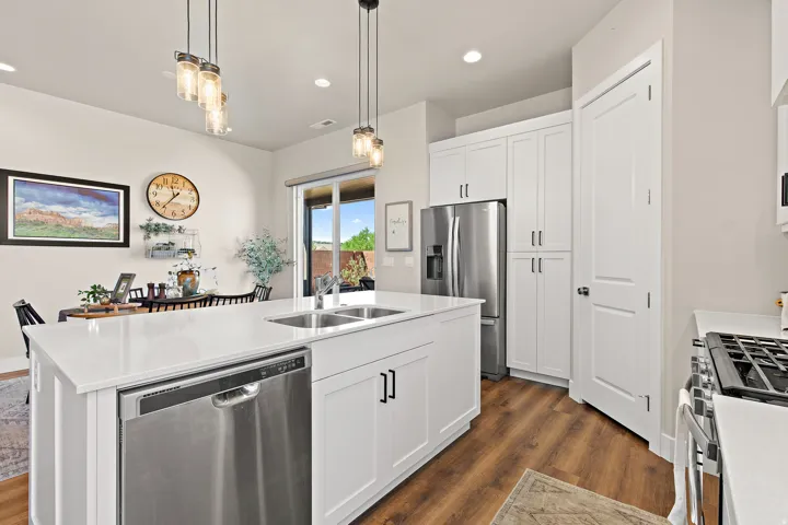 White cabinetry with dark hardware, stainless steel appliances, wood-finish flooring, white countertops, and glass pendant lighting