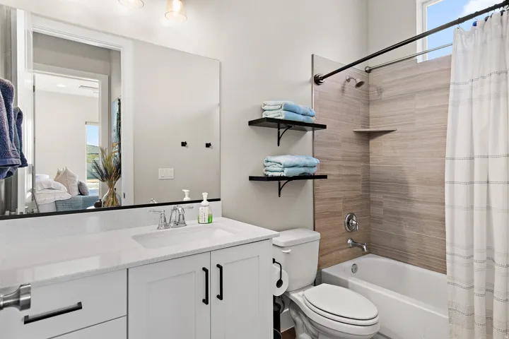White shaker-style vanity with dark hardware, a rectangular undermount sink, and a light-toned countertop