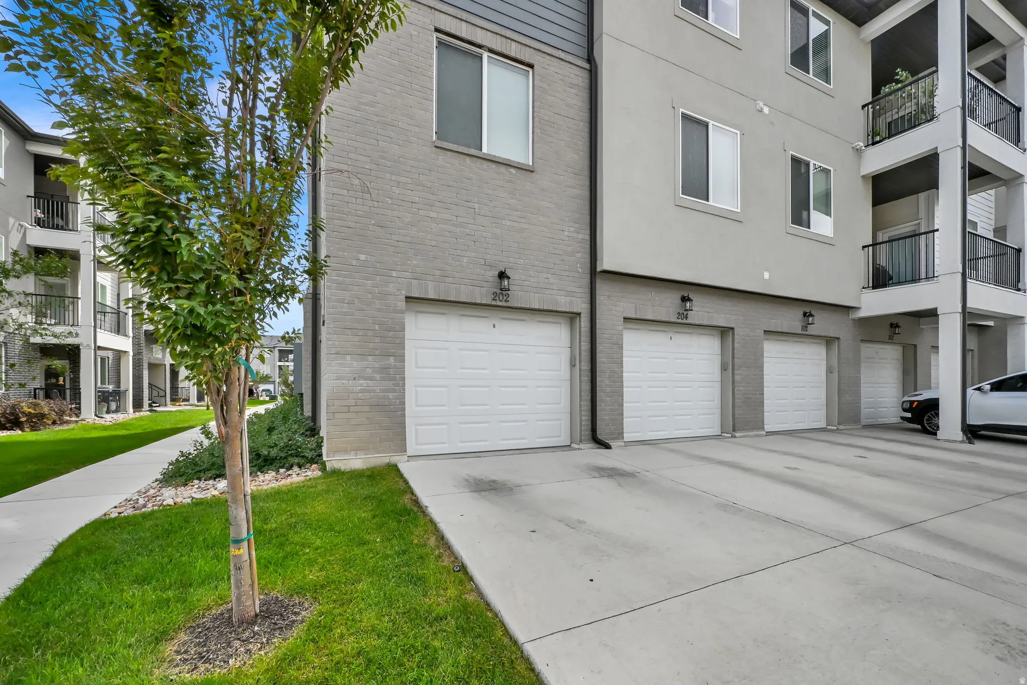 Building exterior featuring brick and stucco siding, multiple white garage doors, private balconies with black railings, and a concrete driveway