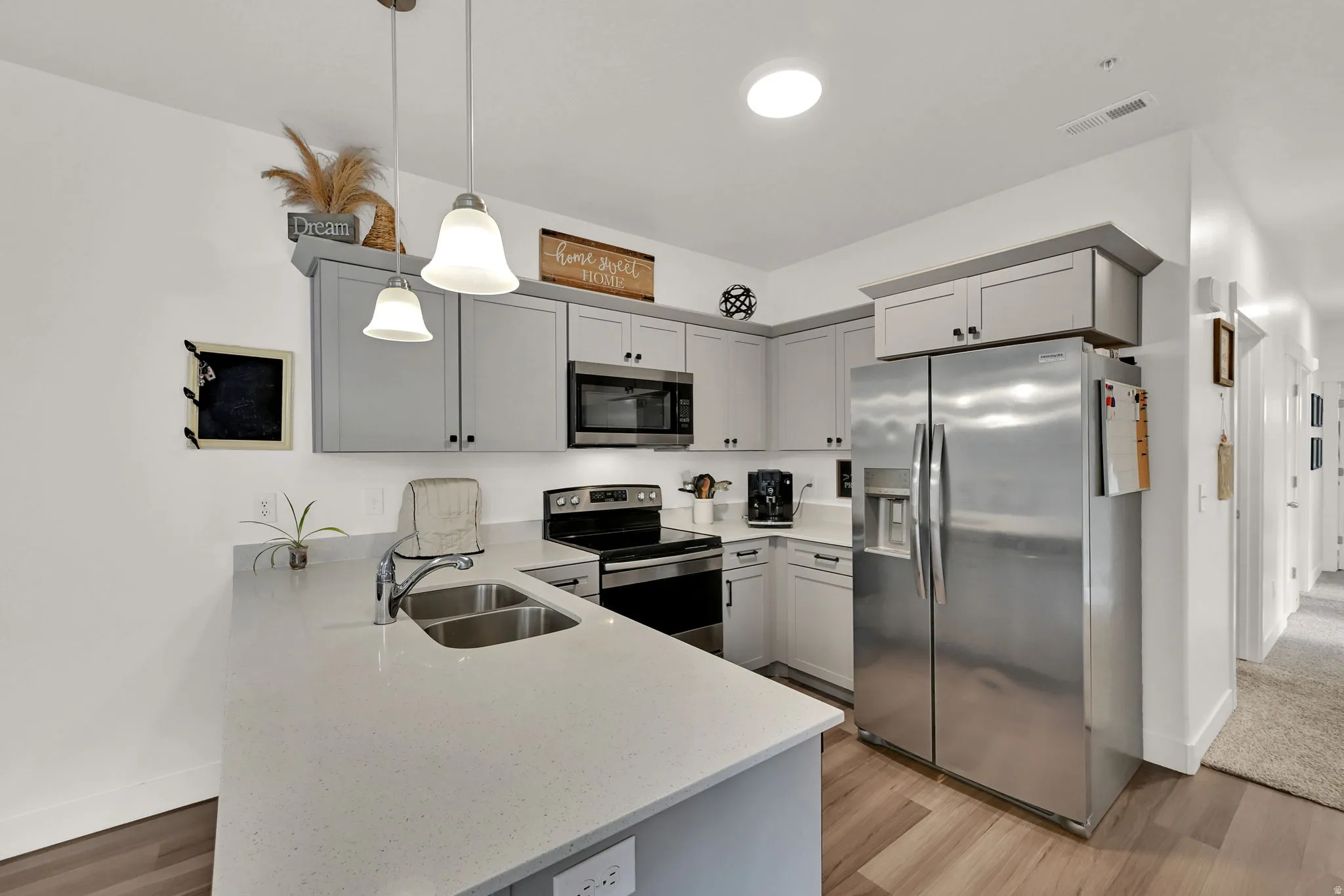 Kitchen featuring light gray cabinetry, stainless steel appliances, light-toned countertops, wood-finish flooring, and pendant lighting