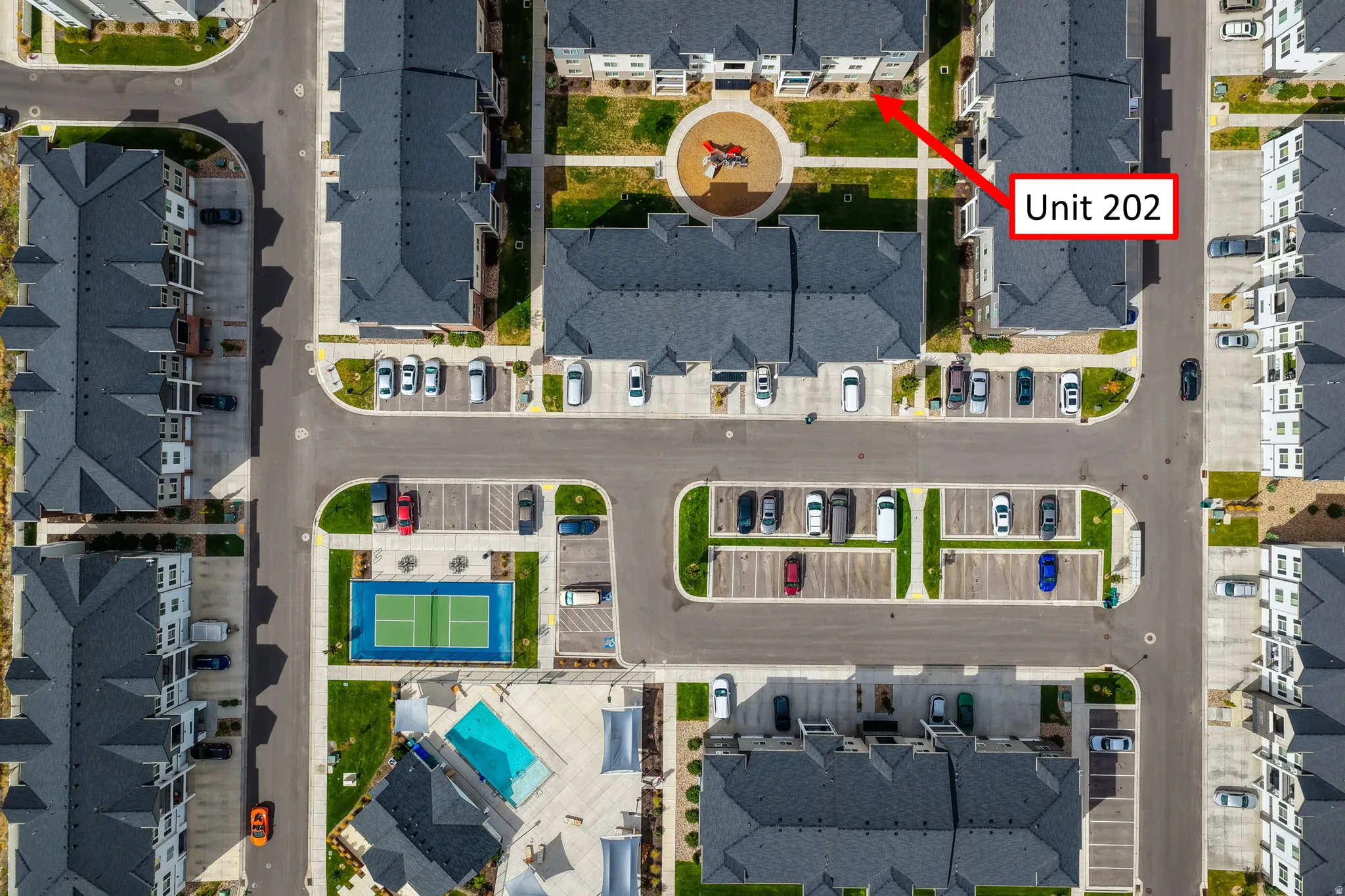 Community with multiple residential buildings, surface parking areas, a central landscaped courtyard, a tennis court, and a swimming pool