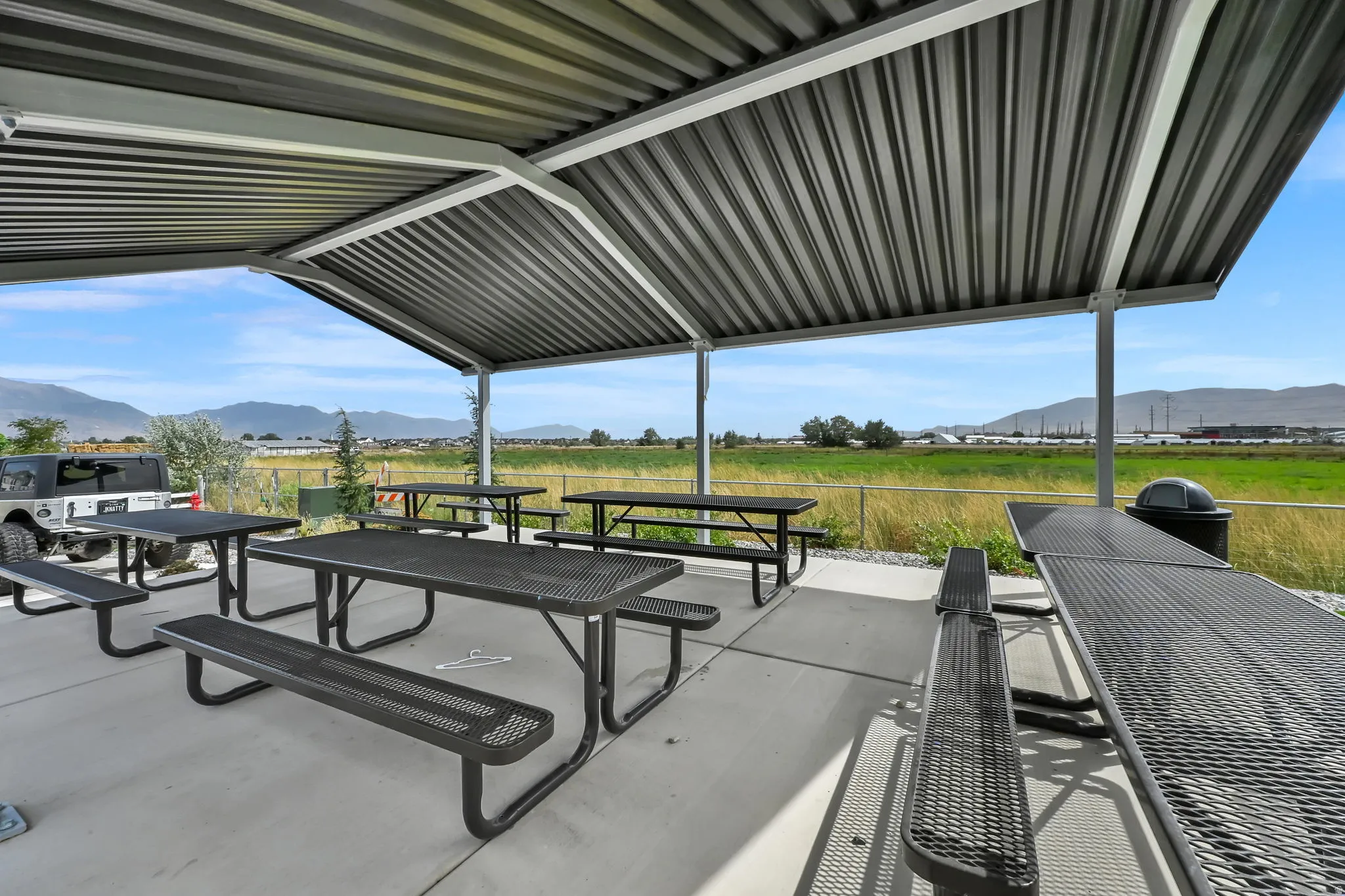 Covered outdoor patio with concrete flooring, multiple picnic tables, and a metal roof structure